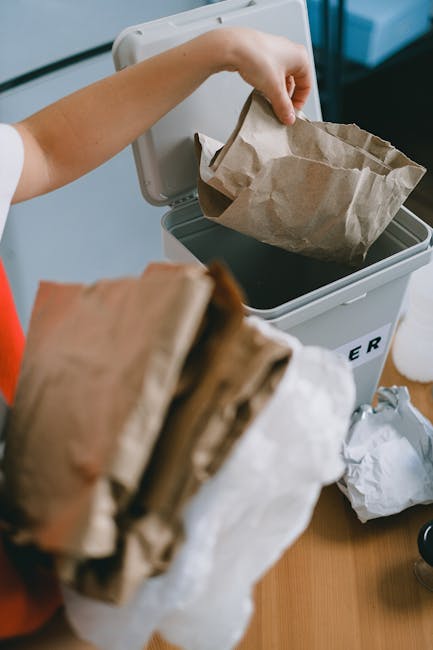 A close-up view of a large pile of crushed and crumpled aluminium and plastic cans, primarily soda cans with bright and metallic finishes, some featuring recognizable brand logos like Coca-Cola. The c